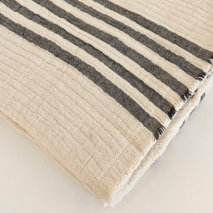 Bruges throw in ecru with black stripes. Lightly quilted layers of cotton gauze with frayed edges finished with a double needle topstitch. 60" l x 50" w.