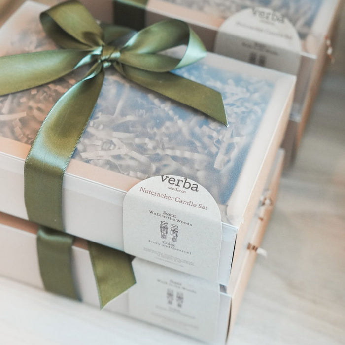 Kraft gift box with green satin bow. Each box contains two scented nutcracker shaped candles. Fragrance is "Walk in the Woods".