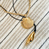 Gold Shell pendant necklace and a gold spiral shell on black cord on a neutral stripe blanket. Each sold separately.