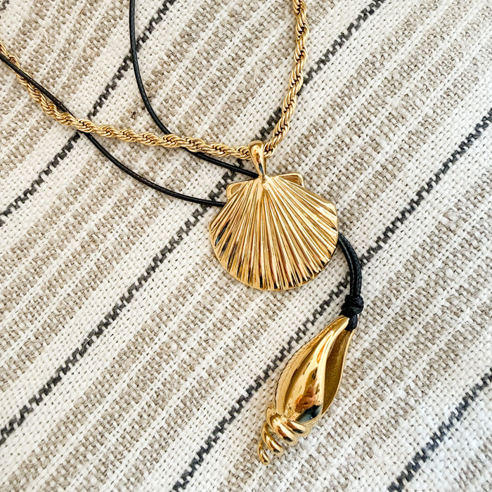 Gold Shell pendant necklace and a gold spiral shell on black cord on a neutral stripe blanket. Each sold separately.