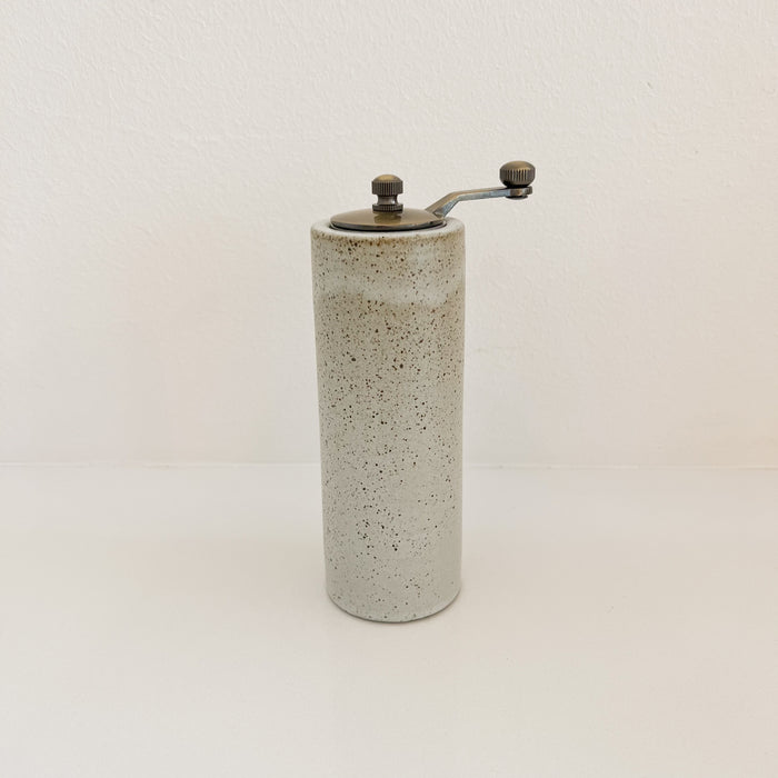 Stoneware peppemill finished in a pale grey glaze with natural brown speckles and topped with a dark bronze handle. Clean cylinder silhouette.