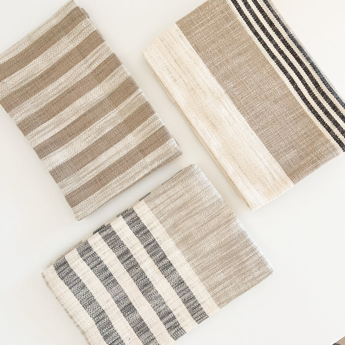 Set of 3 Mesa stripe hand towels in a palette of cream, tan and black. Woven in a 100% cotton hopsack. One tan and cream stripe towel. One cream, sand & black ticking stripe towel and one sand, cream and black cabana stripe towel. Each measures 28" x 18".