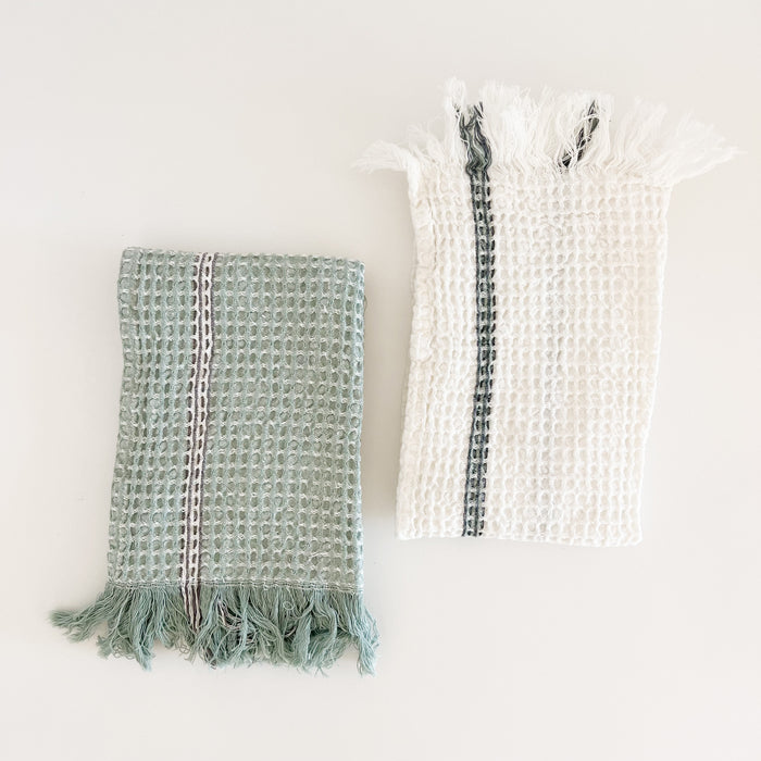 Set of two Rosemary waffle hand towels. 100% cotton with fringe ends. One white towel with sage green and grey stripe, one sage green towel with white/grey stripe. Measures 28" x 18"