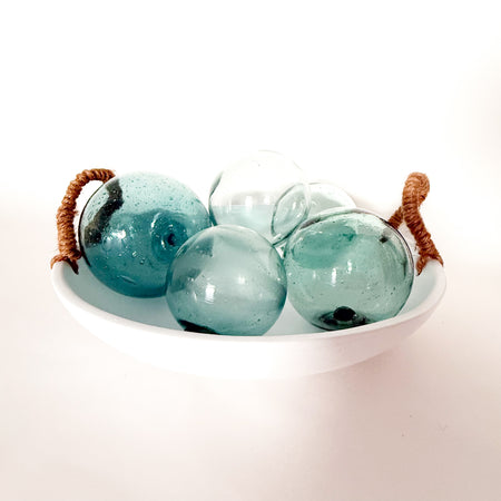 White cement bowl with natural jute handles containing four turquoise glass balls. Balls and bowl sold separately.