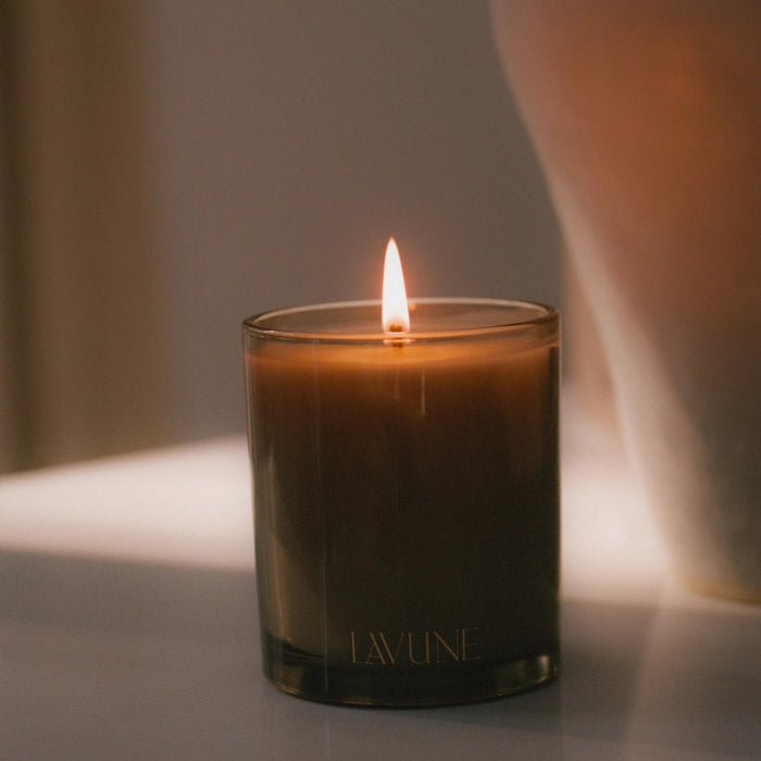 Santal scented candle in a taupe glass container with LAVUNE branding, softly lit with a blurred background.