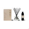 L'AVANT Ambre Santal diffuser set. Includes taupe box packaging, clear glass bottle with black reed diffusers and black bottle of the diffuser fragrance.