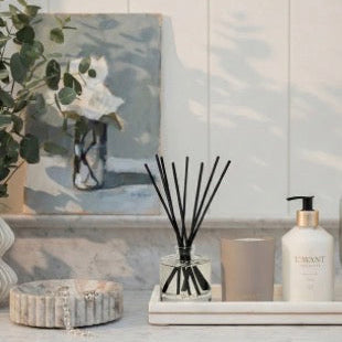 L'AVANT Amber Santal reed diffuser, candle and hand lotion styled on a tray with other decorative objects. Each product sold separately.