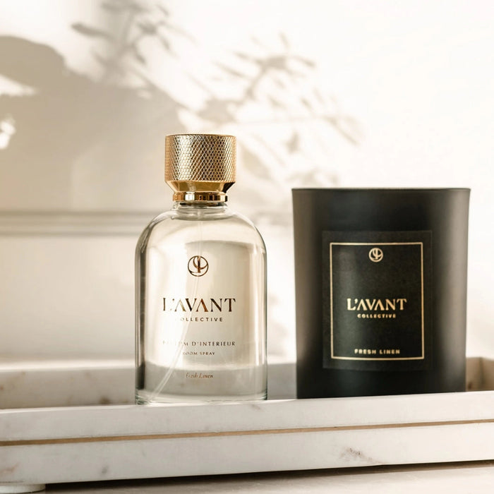 L'AVANT Fresh Linen room spray bottle  and candle on a marble tray with soft dappled lighting. Each sold separately.
