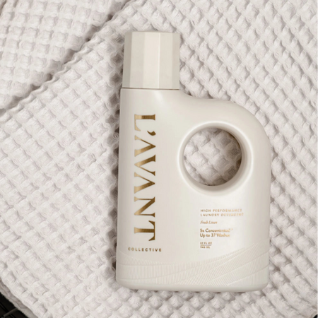 Beige bottle with gold type containing L'AVANT laundry detergent on taupe waffle towel. Fresh Linen fragrance. 32 fl oz./ 946 ml