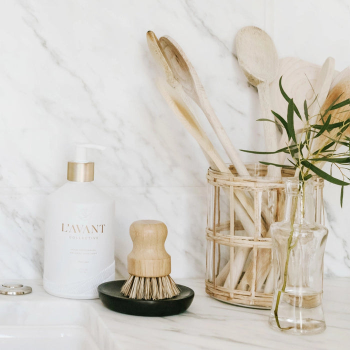 Cleaning supplies including a bottle, brush, and plant on a white surface
