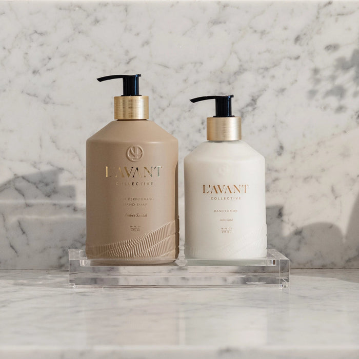 Two bottles on clear lucite tray. One bottle of L'AVANT hand soap, one bottle of L'AVANT dish soap in Ambre Santal fragrance. Each sold separately.