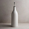 A large white stoneware oil cruet with a speckled glaze and silver metal spout sitting on a beige counter. 12 inch tall, 3.25 inch diameter.