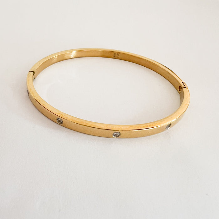 The Lauren Bangle. A delicate gold plated bangle with clear CZ stones inset. Oval shape with hinged clasp, ideal for slim wrists. Made of hypoallergenic stainless steel with 14k gold plating and special finish. Water, sweat and tarnish resistant.