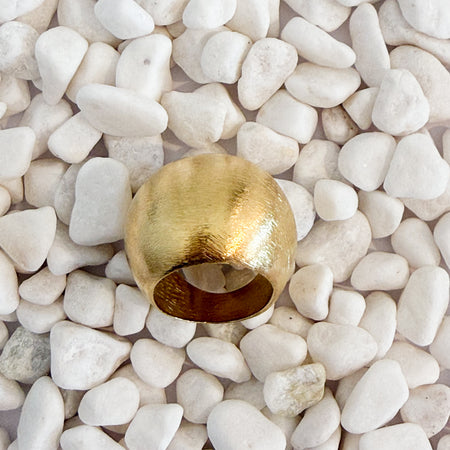 A bold domed ring with a brushed gold finish on white pebbles. 18k gold over brass.