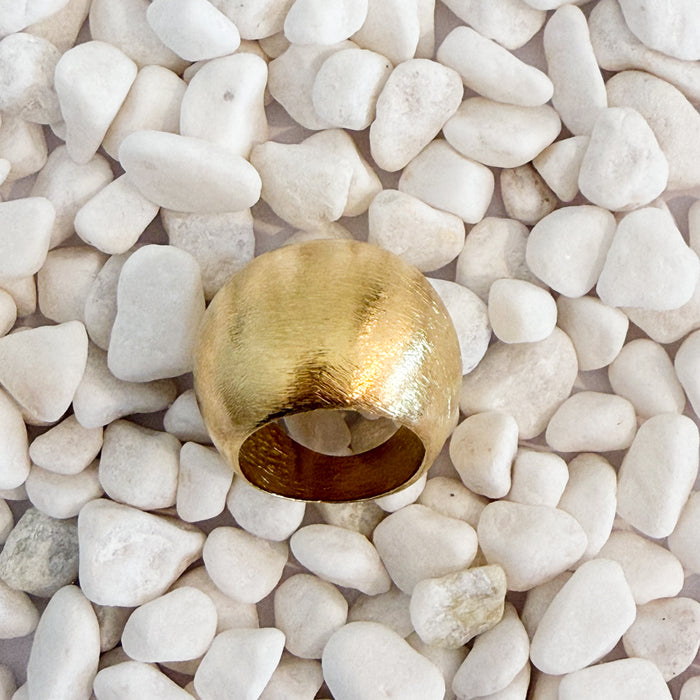 A bold domed ring with a brushed gold finish on white pebbles. 18k gold over brass.