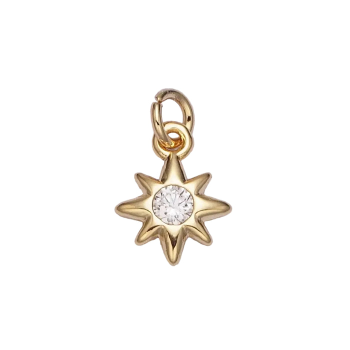 Gold star-shaped charm pendant with a central clear CZ gemstone on white. background. 16K gold plated over brass.