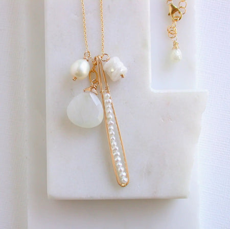 Moonstone cluster necklace. 20" gold filled chain with four charms, a large faceted Moonstone, a small stack of Moonstones, a white pearl and a stack of seed pearls on a gold threader. Handcrafted in Northern California.