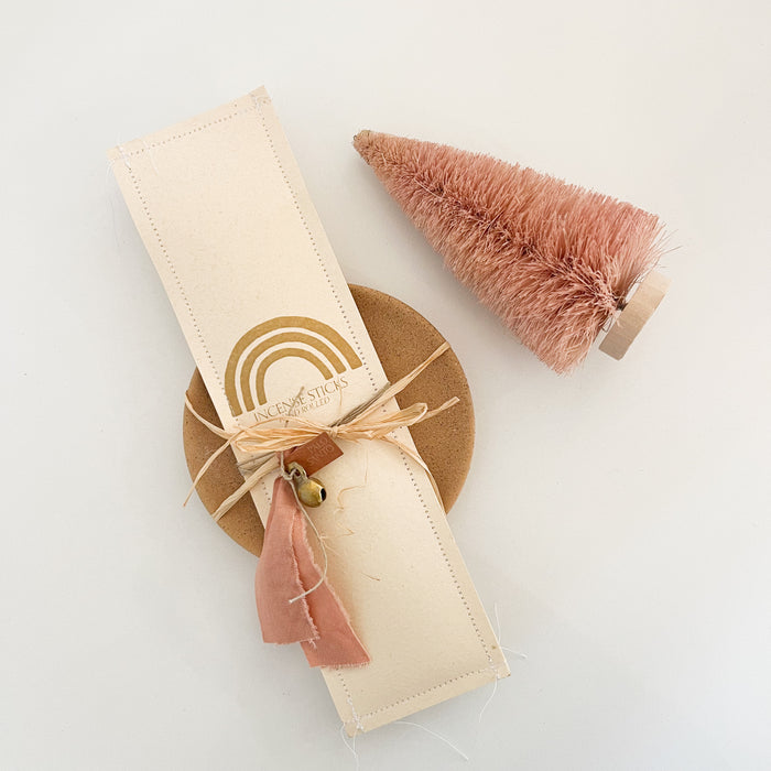 Package of 12 hand rolled Palo Santo incense sticks with a raw terra cotta incense dish. Incense is packaged in a hand crafted paper envelope wrapped with a blush ribbon and brass charm.