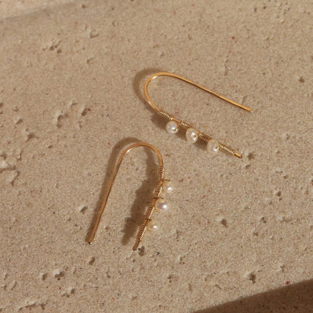 Pair of 14K gold filled arch earrings threaded with 3 small pearls on tan travertine tray. 1.5 inch length.