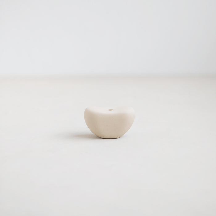 The Pod candle holder, part of the Pebbles collection designed to hold the slim Wish taper candles (sold separately). Organic ceramic form inspired by beach pebbles with a matte white glaze. 2.5" diameter x 1.25" tall.