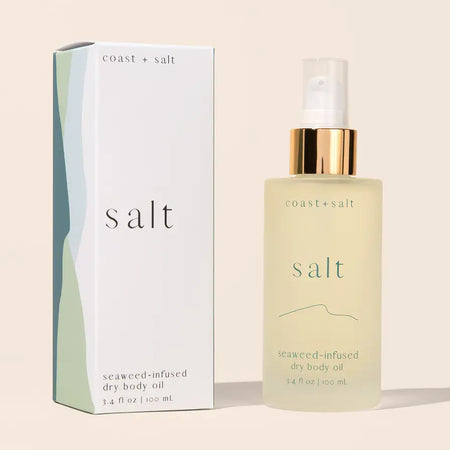 A spray bottle of Coast + Salt seaweed-infused dry body oil next to its white packaging box with abstract green and blue-gray wave designs. 3.4 fl oz/100mL.