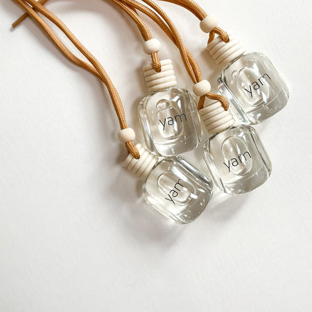 Four clear hanging bottles of SAND citrus-amber diffuser with neutral cord. 