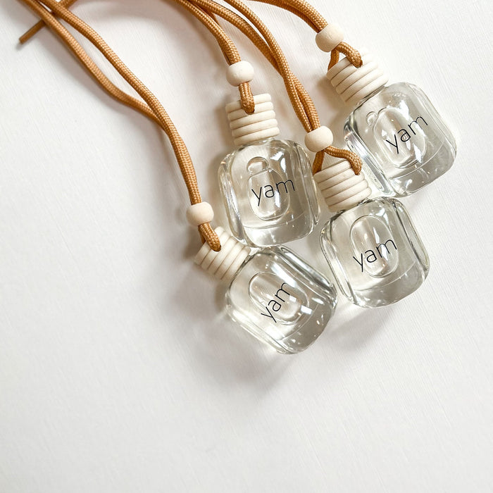 Four clear hanging bottles of SAND citrus-amber diffuser with neutral cord. 
