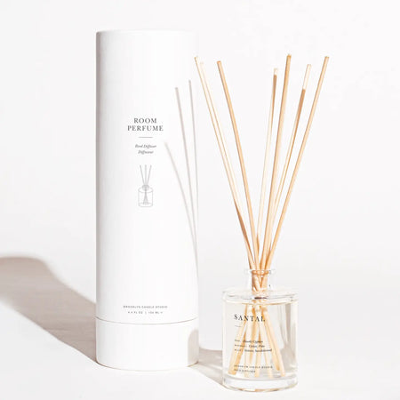 Santal Reed Diffuser by Brooklyn Candle Studio. Santal is a sultry fragrance blend of earth and woods. Packaged in an ivory matte paper tube containing Santal fragrance oil in clear glass bottle, natural wood stopper and 8 rattan reeds. Lasts approximately 4-5 months. 4.4 fl oz/ 130 ml.