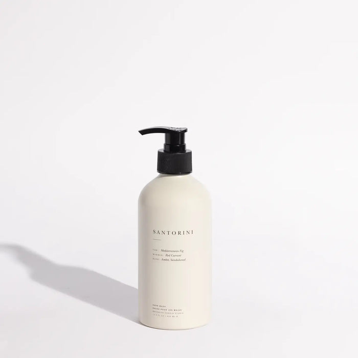 Santorini Hand Wash in a matte cream aluminum bottle with black pump and minimalistic typography. Luxurious fragrance with base notes of Amber and Sandalwood, mid note of Red Currant and top notes of Mediterranean Fig. 13.5 oz/ 400ml. Made in the USA.