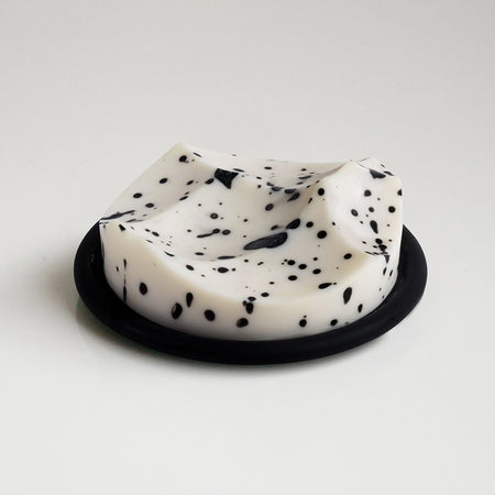 White soap bar with black specks on a black soap dish against a light gray background. White Grapefruit fragrance. 