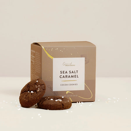 Box of sea salt caramel cocoa cookies with two cookies in front on a light background