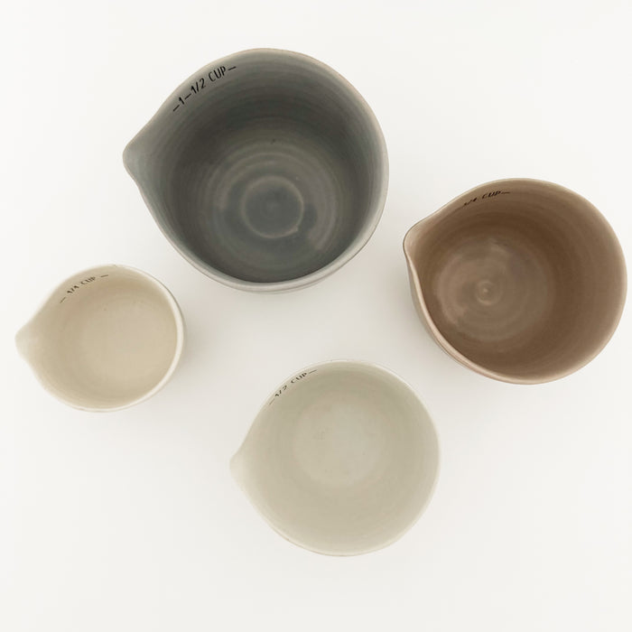 Set of four neutral ceramic measuring cups in mineral grey, terra cotta, taupe and cream with hand shaped spout. 
