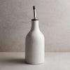 Small white stoneware oil cruet with a speckled glaze and silver metal spout sitting on a beige counter. 9 inches tall, 3 inch diameter.
