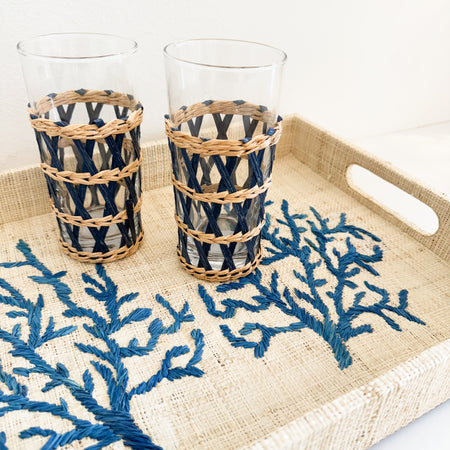 Southport Tray shown with two Newport Cane glasses. Each sold separately. Tray features a hand embroidered coral design in a rich blue on a natural raffia base. Measures 16 x 12 x 2 inches.