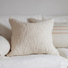 A square ivory throw pillow with a textured boucle surface, styled on a white sofa with other neutral-toned pillows in the background. Each pillow sold separately.