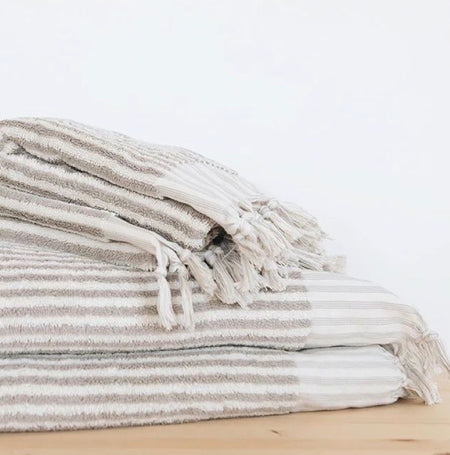 Stack of striped taupe and white towels on a light wooden surface.