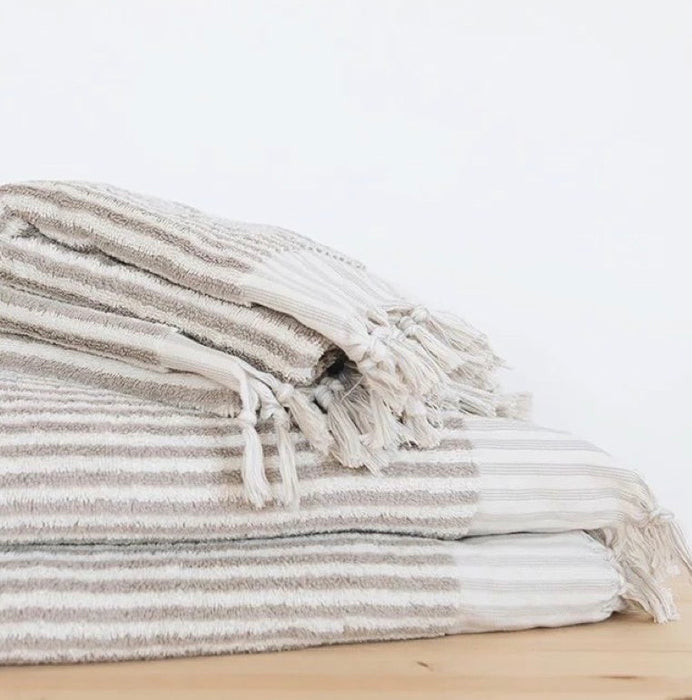 Stack of striped taupe and white towels on a light wooden surface.