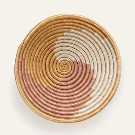 Top view of a round basket bowl constructed of coils of natural sweetgrass with a swirled graphic pattern in ivory and blush pink. 12 inch diameter x 3 inch depth.