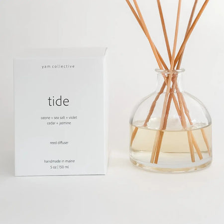 TIDE reed diffuser, in a clear bottle with natural rattan diffuser sticks next to a white box with TIDE by Yam Collective. Fragrance notes of Citrus, Jasmine, Violet and Cedar. 5 fl oz.