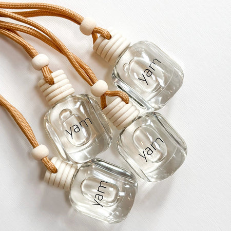 Four small hanging glass bottles of TIDE jasmine-cedar diffuser oil with a neutral cord and YAM branding. 
