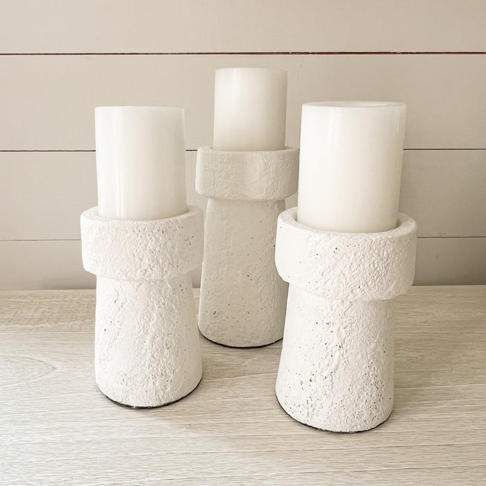 Three Tulum candle holders with white pillar candles. Modern silhouettes formed in from rustic stoneware with a matte white lava stone finish. Candle holders and pillars sold separately.