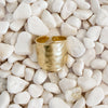 A bold hammered gold ring with a wide, open band, resting on a bed of smooth white pebbles. Adjustable, fits size 7-9. 18k gold over brass.
