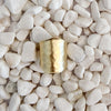 A bold hammered gold ring with a wide, open band, resting on a bed of small white pebbles. Adjustable, fits size 7-9. 18k gold over brass.