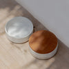 Set of two Wabi stoneware ramekins. Stackable round containers with one natural wood lid. Made of sand specked stoneware with a creamy white  glaze. l4" diameter, each dish is 1.5" high, 3.25" total when stacked with lid.