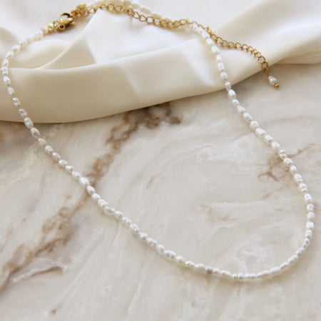 Delicate choker necklace with tiny white fresh water pearls. 15.5 inch length with 4 inch extender. Natural freshwater pearls with 18k gold over surgical steel fittings. Water and tarnish resistant.