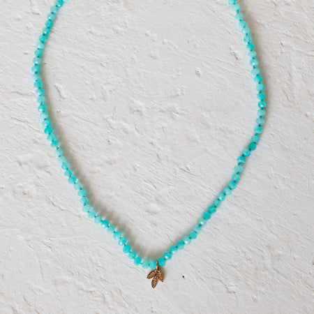 Sea Palm Necklace. Small aqua blue Amazonite beads strung together with a golden palm frond charm encrusted with clear CZ stones. Measures 15" length with a 3" extender.
