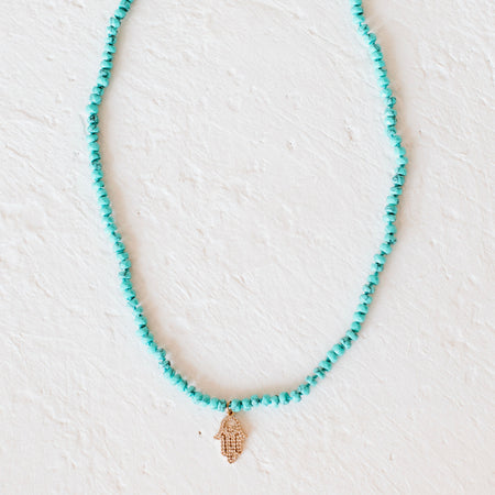 Turquoise Hamsa Charm Necklace. Small genuine turquoise stones strung together with a delicate golden Hamsa hand pendant. Pendant is encrusted with clear CZ stones. Measures 15" length with 3" extender.