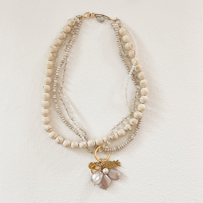 Peace + Love Charm necklace by Bittersweet Designs. 16" length when double wrapped. Made of multiple strands of bone beads, semi precious quartz and moon stones. Finished with an eclectic cluster of charms suspended from a 14k gold plated ring.