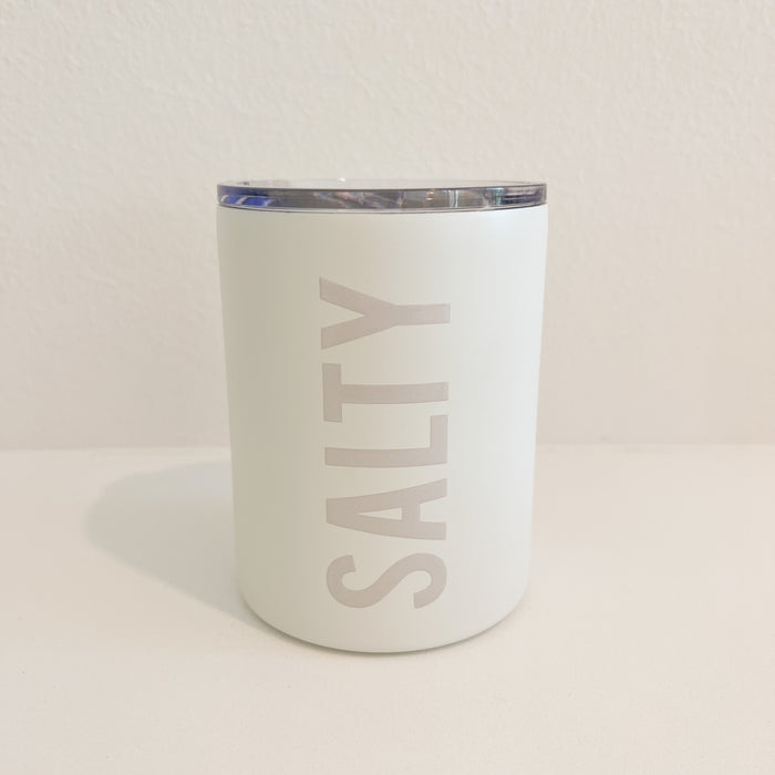 SALTY stainless steel insulated tumbler with clear sip lid. Exterior is coated in a matte white enamel with glossy cream letters spelling "SALTY". Holds 12 fl ounces.