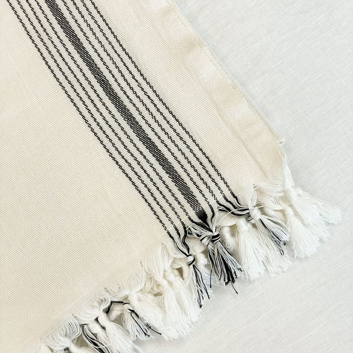 The Malibu Bath Towel is luxuriously oversized, worthy of a spa. Measures 33"W x 74"L. Made in Turkey on traditional looms in 100% cotton. Unbleached natural cream color is framed with a cluster of thin black stripes on each side. Hand knotted tassels finish off the ends.